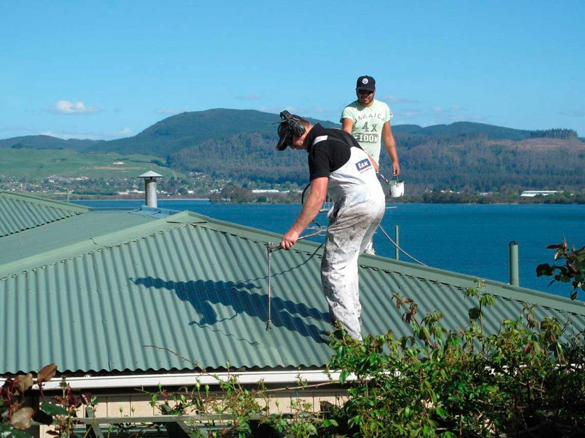 Shane Green and assistant on a roof spraying or recoating the roof.